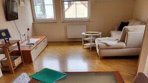 Una habitación con una mesa de vidrio grande, un sofá, una mesita redonda y un televisor montado en la pared.