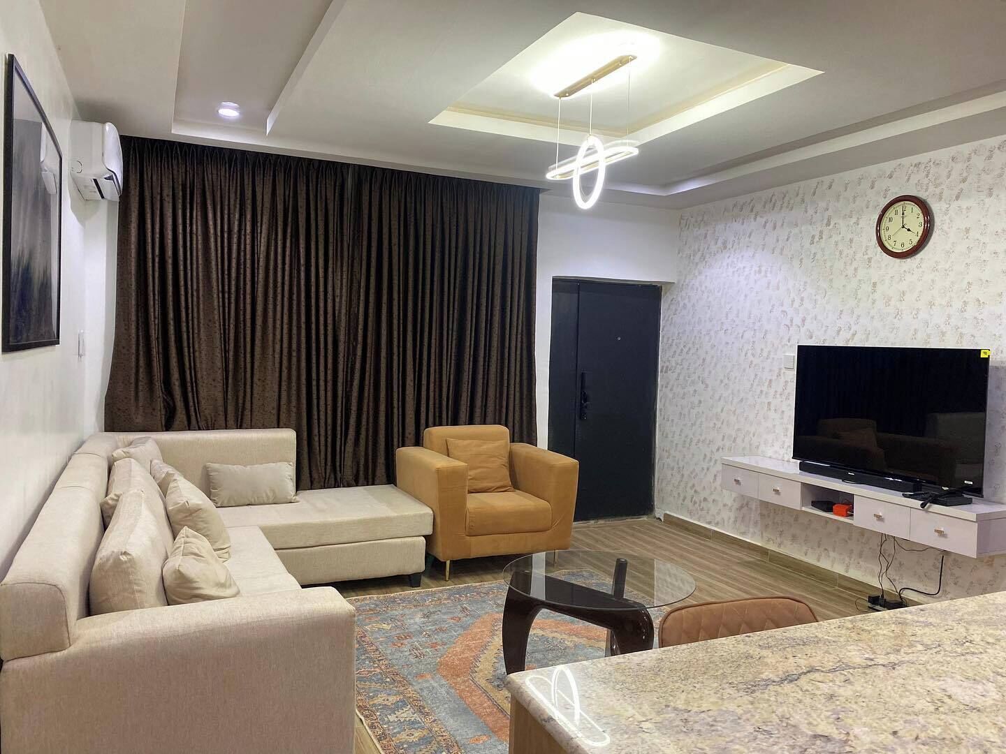 A modern living room with a sofa, armchair, TV, and a glass coffee table.
