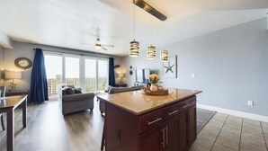 A modern kitchen with a central island, a dining area with a sofa, and a large window with curtains.