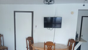 A dining area with a round wooden table and four chairs, a ceiling fan, and a mounted flat-screen TV. - Cozy hotel suite in peaceful Mayo with AC, WiFi, fitness room (Mayo)