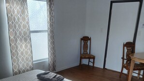 A bedroom with a wooden bed, two chairs, a small table, and a window with patterned curtains. - Cozy hotel suite in peaceful Mayo with AC, WiFi, fitness room (Mayo)