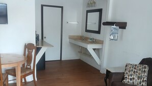 A living room with a wooden floor, a brown sofa, a dining table with a chair, a kitchen area with a sink and mirror, and a ceiling fan. - Cozy hotel suite in peaceful Mayo with AC, WiFi, fitness room (Mayo)