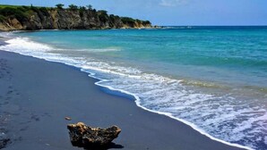 Una playa con arena oscura, una roca al frente y un mar tranquilo.