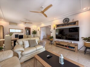 A modern living room with a sofa, coffee table, TV, and ceiling fans. - Villa Claudia by Hello Homes Sitges (Sitges)