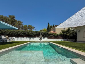 A swimming pool with a clear blue water, surrounded by a well-maintained lawn and a white fence. - Villa Claudia by Hello Homes Sitges (Sitges)