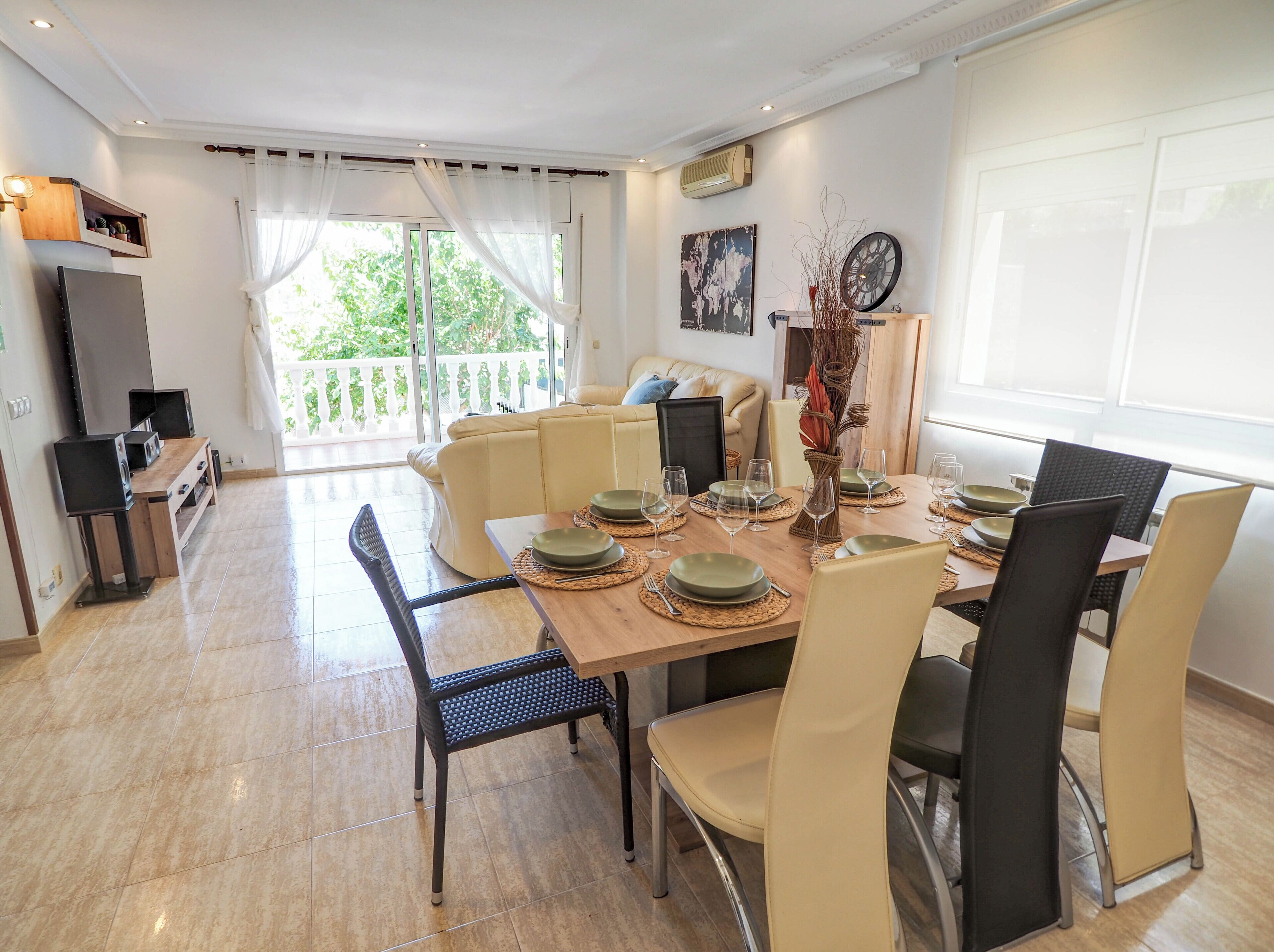 A dining area with a wooden table set for four, surrounded by chairs, and a sofa in the background.