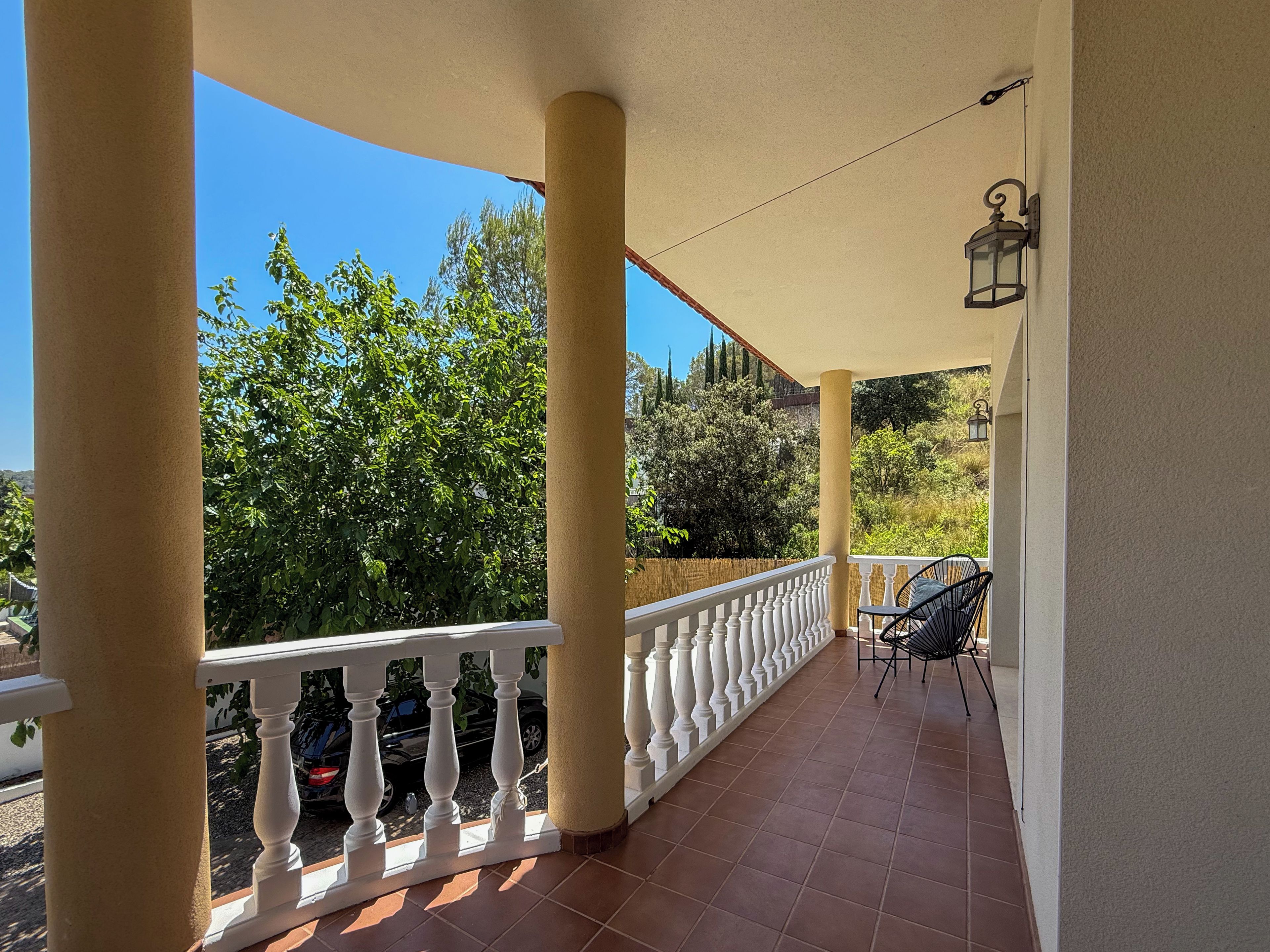 A covered balcony with a white balustrade, a chair, and a hanging lantern.