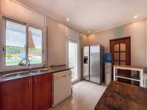 Eine moderne Küche mit eingebautem Geschirrspüler, einem Kühlschrank und einem Fenster mit Blick auf einen Garten.