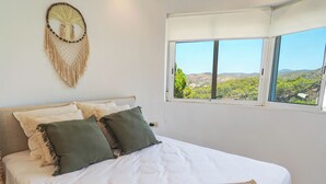 Een slaapkamer met een bed, uitzicht op een landschap door een raam en een wanddecoratie.