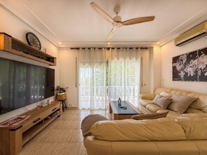 A living room with a television, sofa, coffee table, and a ceiling fan. - Villa Claudia by Hello Homes Sitges (Sitges)