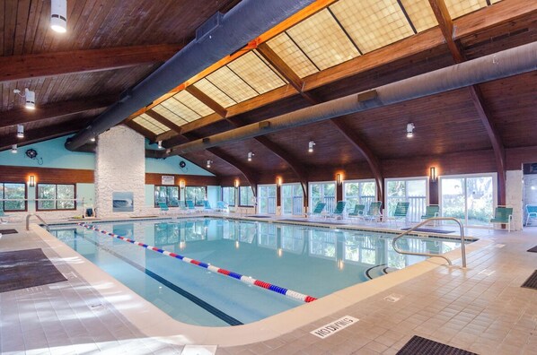 An indoor swimming pool with a wooden ceiling, clear windows, and lounge chairs.