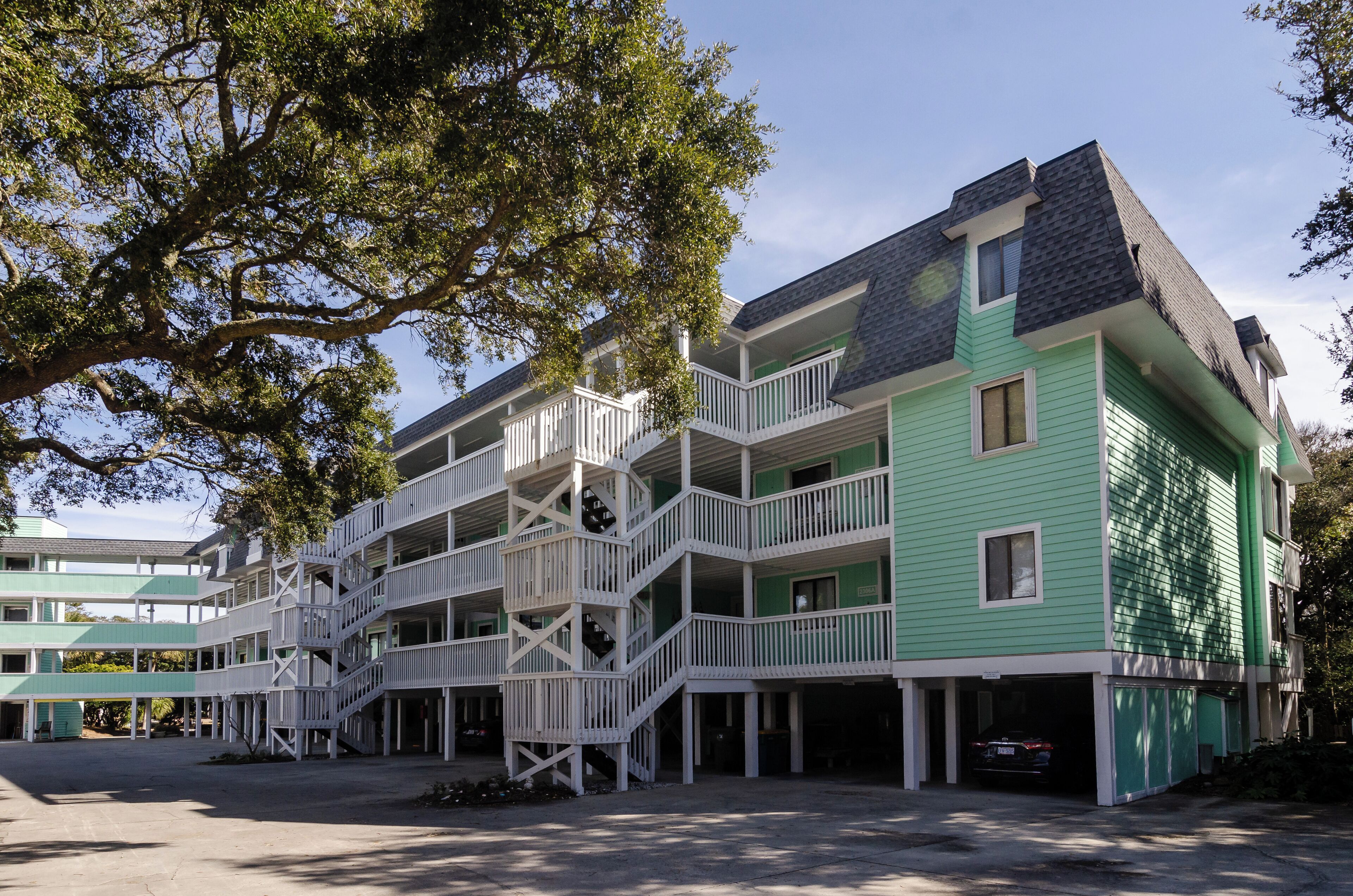Ein mehrgeschossiges Gebäude mit grüner Fassade und weißen Balkonen, mit einer zentralen Treppe und einem Parkplatz.