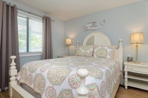 Un dormitorio con cama, dos mesitas de noche, una ventana con cortinas y una decoración en la pared.