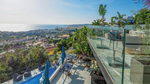 Eine Dachterrasse mit Pool, Sitzbereichen und einer Glasbrüstung mit Blick auf Stadt und Meer.
