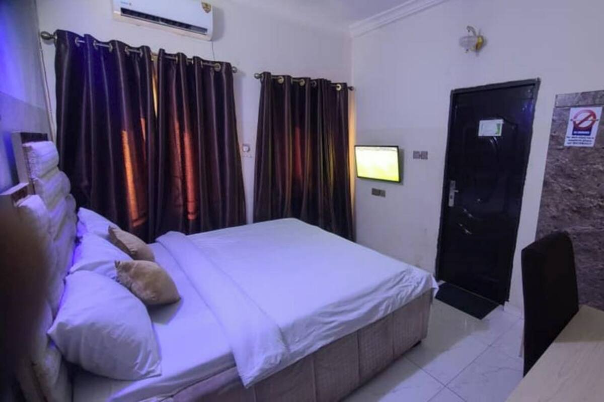 Una habitación de hotel con cama, cortinas, televisor, puerta y aire acondicionado instalado en la pared.