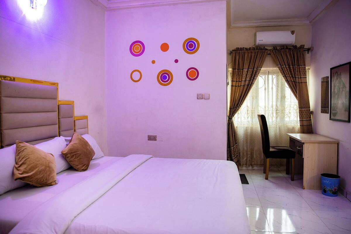 Habitación de hotel con cama, escritorio, silla, pared con diseños circulares y aire acondicionado.