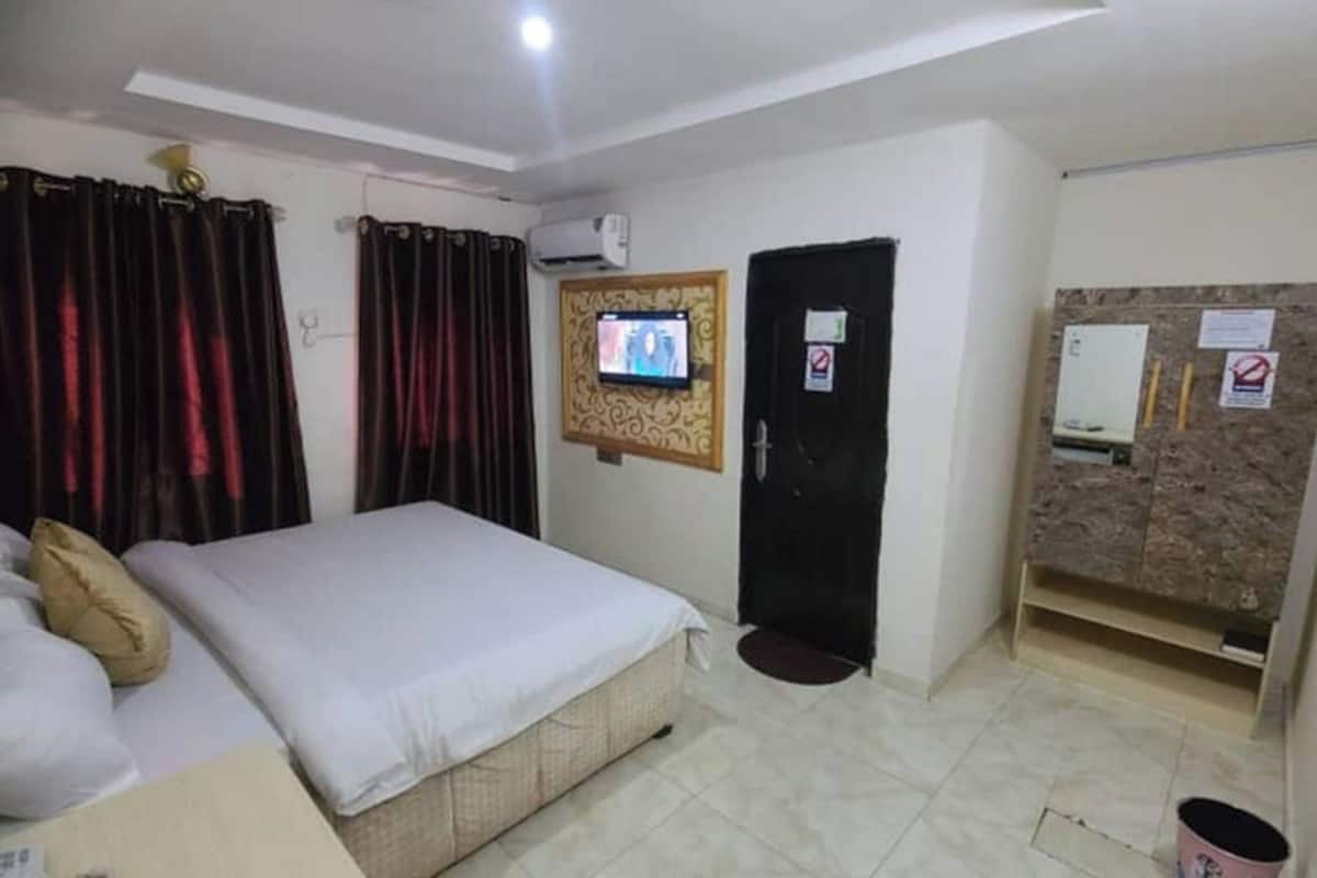 Una habitación de hotel con una cama, cortinas, televisión, puerta y un tablón de anuncios.