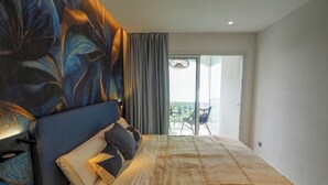 A bedroom with a large bed, a headboard with a floral design, a balcony with a table and chairs, and a view of the outside. - Blue Suite by Hello Homes Sitges (Sitges)
