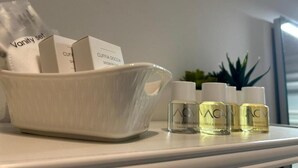 Un meuble-lavabo de salle de bain avec un vasque blanc contenant une serviette blanche et une boîte étiquetée « Ensemble de produits de beauté ». Trois flacons de gel douche et de shampoing sont posés sur le comptoir.