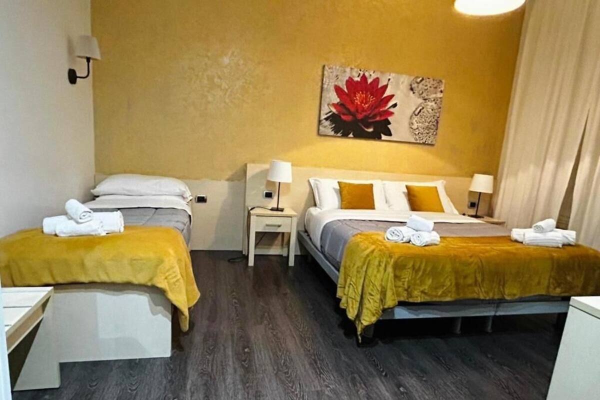 A room with two beds, each with a yellow bedspread and white pillows, a nightstand with a lamp, and a painting on the wall.