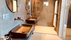 A modern bathroom with a long vanity, two sinks, a mirror, and a shower area.