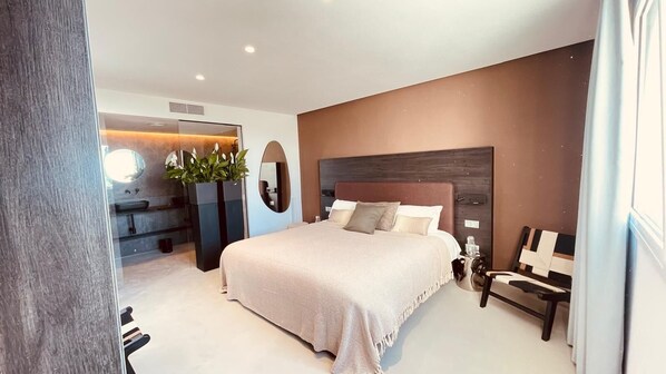 A modern bedroom with a large bed, a bedside table, a mirror, and a plant. - Wengé Suite by Hello Homes Sitges (Sitges)