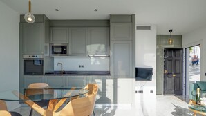 Una cucina moderna con mobili grigi, un tavolo da pranzo in vetro, sedie in legno e una TV a parete.