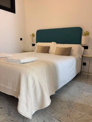 Una cama bien hecha con un cabecero verde azulado, ropa de cama blanca y una manta color beige.