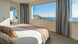 A bedroom with a large window, a bed with a blanket, and a view of a coastal landscape. - Pink Suite by Hello Homes Sitges (Sitges)