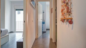 A hallway with a tiled floor, a bed with a white cover, a wall-mounted decorative shell piece, and a door leading to another room. - Central Terrace by Hello Homes Sitges (Sitges)