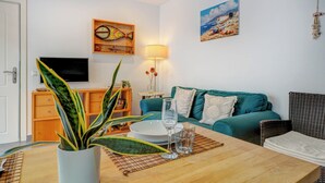 A living room with a teal sofa, a wooden coffee table, a potted plant, a painting of a beach scene, and a television on a wooden cabinet. - Central Terrace by Hello Homes Sitges (Sitges)