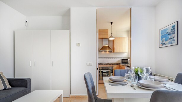 A modern living room with a dining area, white furniture, and a kitchen in the background. - Ribes Duplex by Hello Homes Sitges (Sitges)
