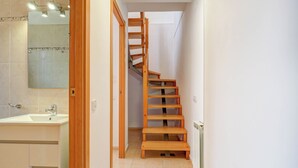 A narrow hallway with a wooden staircase leading to a landing. A bathroom with a sink and mirror is visible on the left. - Ribes Duplex by Hello Homes Sitges (Sitges)
