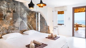Quarto moderno com uma cama grande, duas mesas de cabeceira e vista para o mar através de uma porta de vidro.