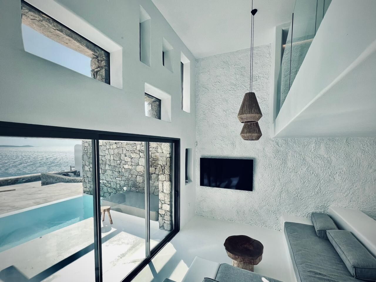 Un soggiorno moderno con una parete in pietra, un'ampia finestra vista piscina e un televisore piatto montato a parete.