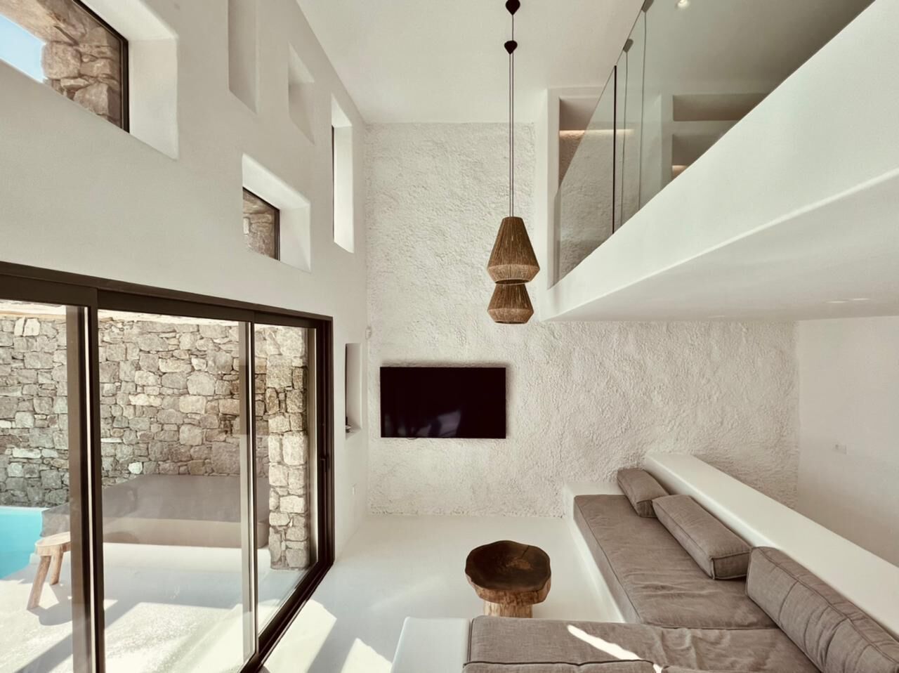 A modern living room with a stone wall, a flat-screen TV, a sofa, and a hanging light fixture.