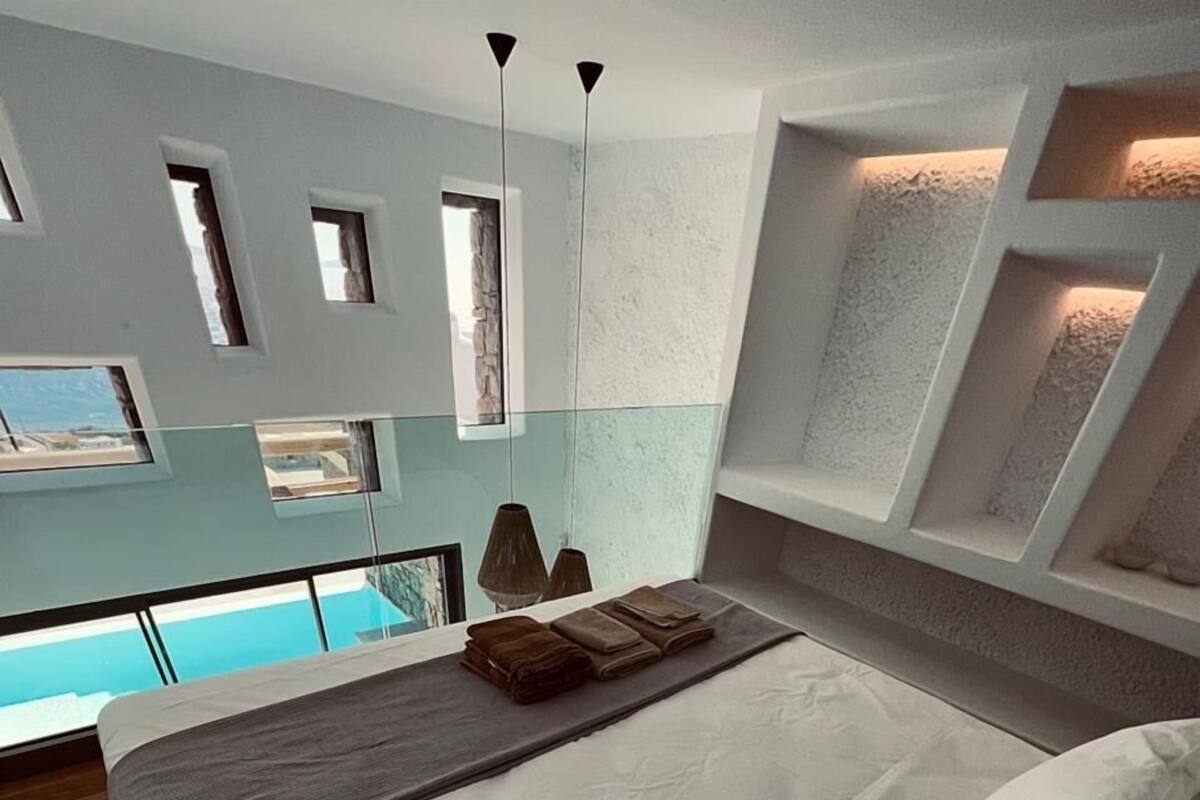 A modern bedroom with a large bed, a glass balcony, and a stone wall.