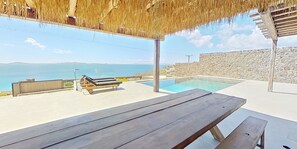 A wooden deck with a pool and lounge chairs, overlooking a stone wall and the sea. - Ria Mar Villas & Suites by Live&Travel (Mykonos)