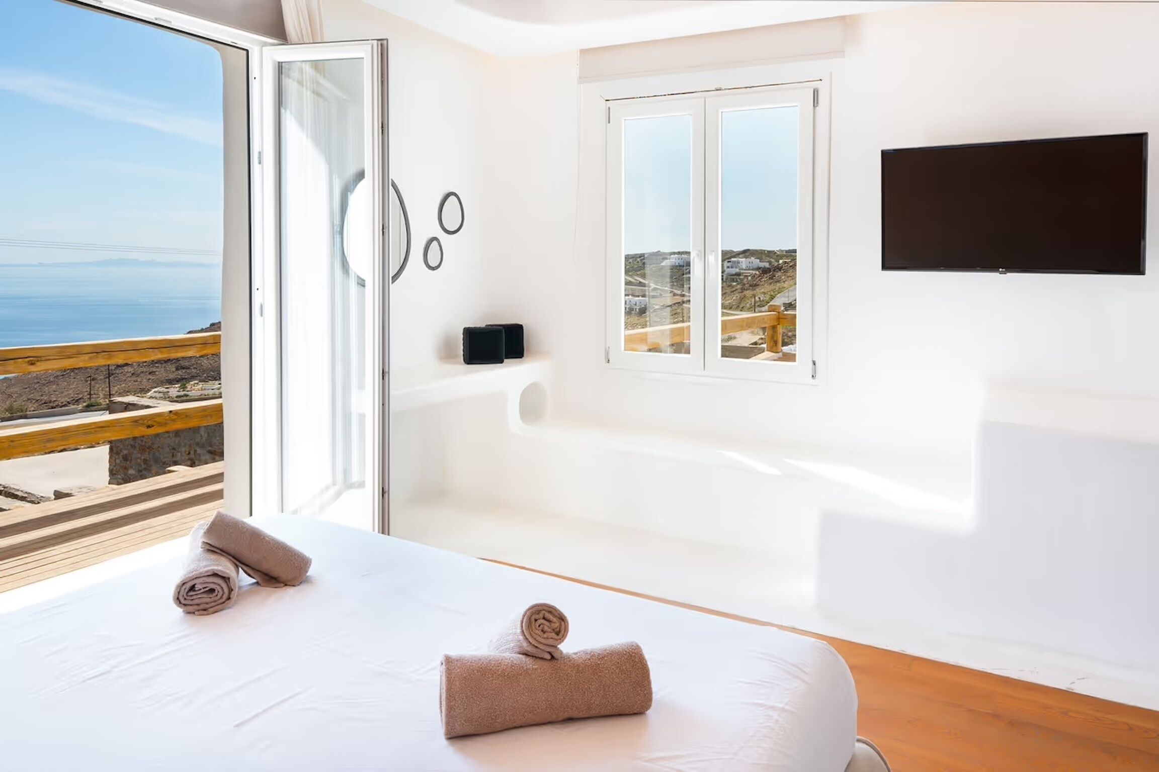 A modern hotel room with a large bed, a bathtub, and a view of the sea.