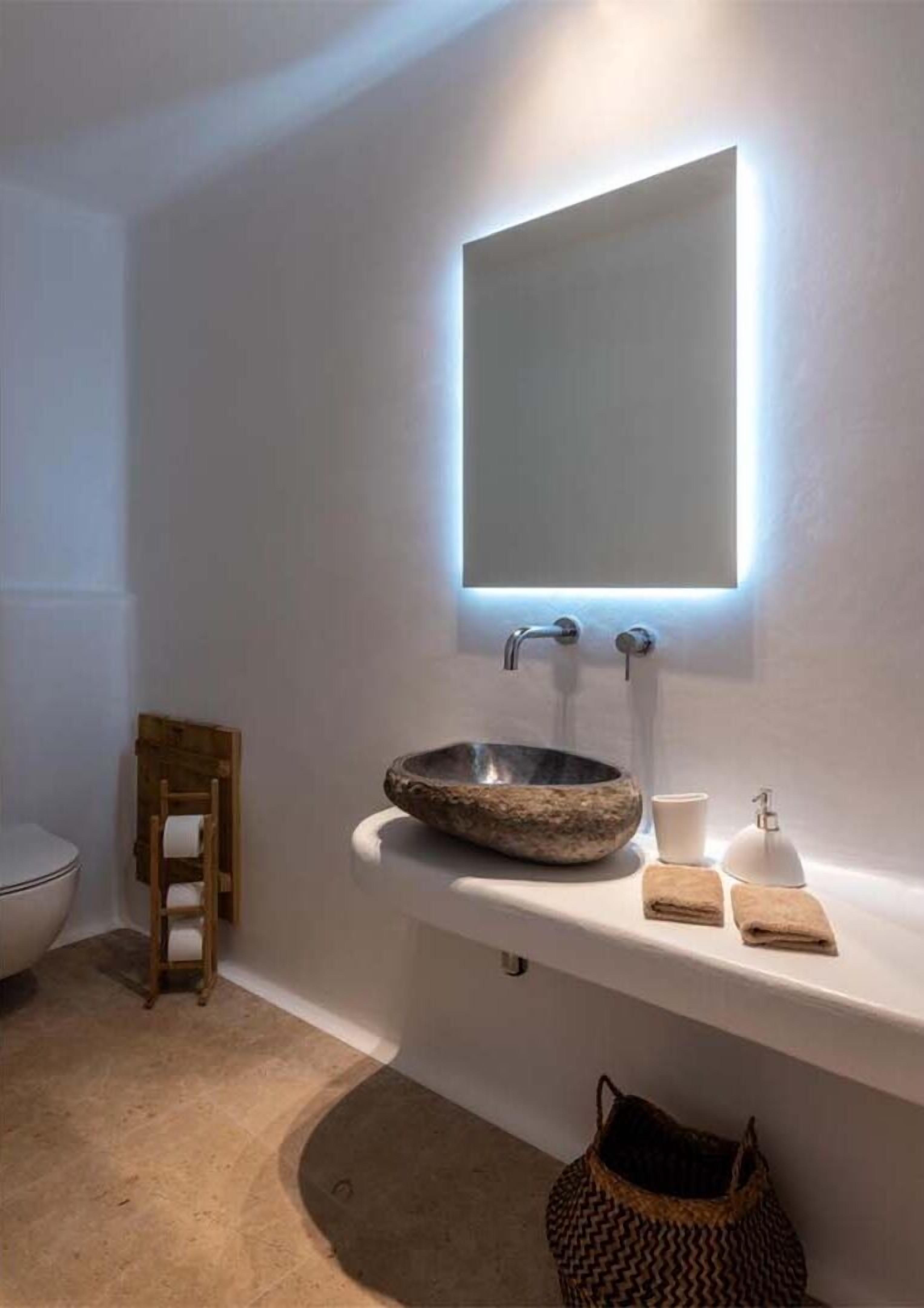 Un baño moderno con un lavamanos de piedra, un espejo y una pequeña silla de madera.