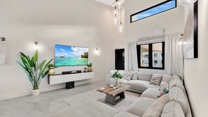 A modern living room with a flat-screen TV, a large sofa, a coffee table, and a potted plant.