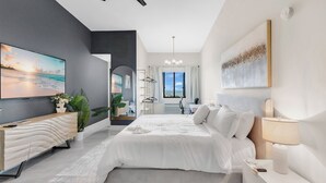A modern bedroom with a large bed, bedside tables, a TV, and a ceiling fan.