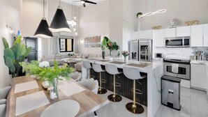 Una cocina moderna con armarios blancos, electrodomésticos de acero inoxidable y una isla central con taburetes de bar.