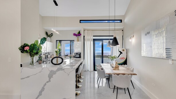 A modern kitchen with a marble island, dining area with chairs, and a view to the outside.