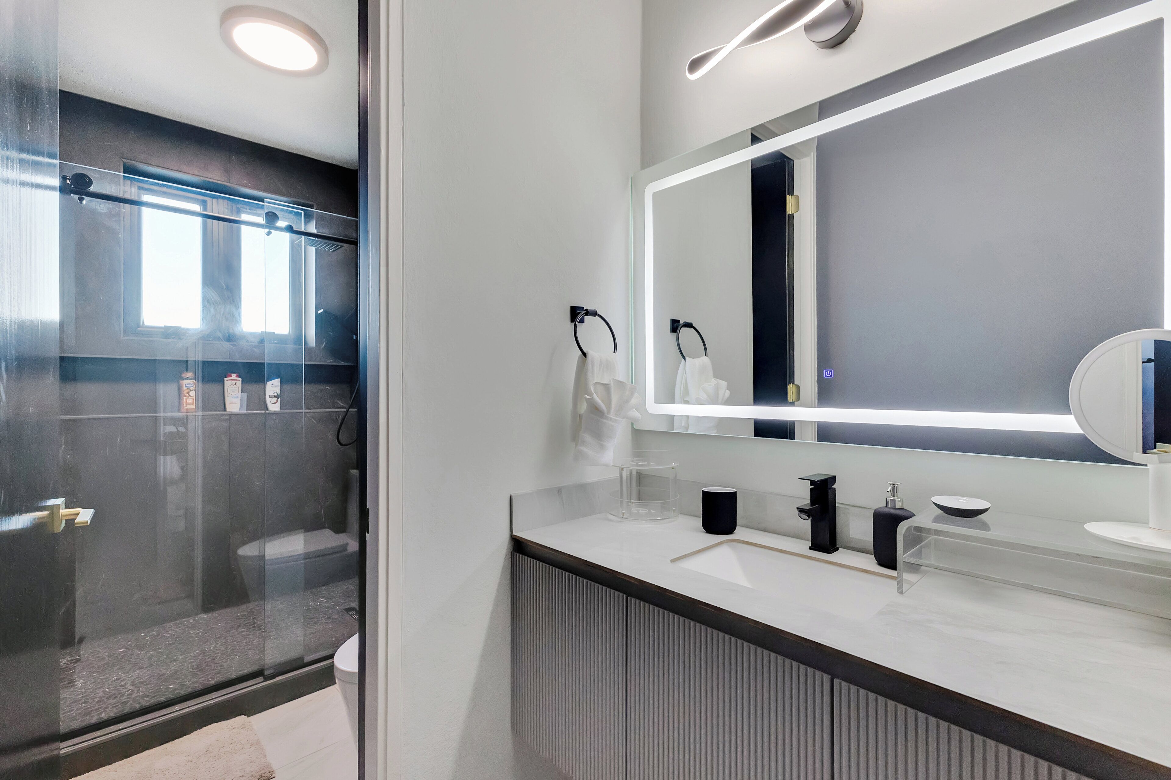 Un baño moderno con un espejo grande, un lavabo blanco y una cabina de ducha con paredes de vidrio.