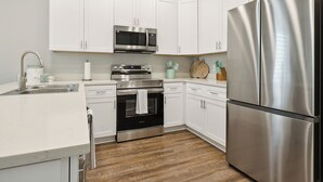 A modern kitchen with white cabinets, stainless steel appliances, a microwave, oven, and a refrigerator. - Waterfront 2-bedroom condo in Slidell (Slidell)