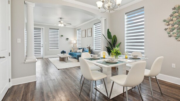 A dining area with a white table set for four, surrounded by white chairs. There is a chandelier above the table and a ceiling fan in the background. - Waterfront 2-bedroom condo in Slidell (Slidell)