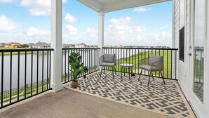 A covered balcony with two chairs and a table, a potted plant, and a view of a body of water and distant buildings. - Waterfront 2-bedroom condo in Slidell (Slidell)