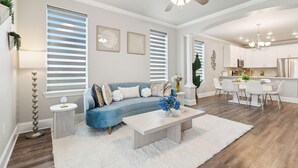 A modern living room with a blue sofa, white coffee table, and a dining area with white chairs. - Waterfront 2-bedroom condo in Slidell (Slidell)