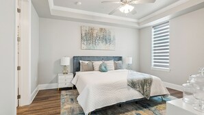 A bedroom with a bed, bedside tables, a ceiling fan, a window with blinds, and a decorative wall piece. - Waterfront 2-bedroom condo in Slidell (Slidell)
